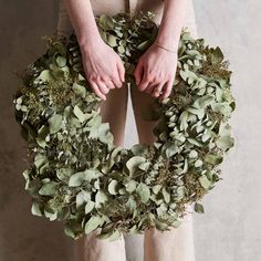 a person holding a wreath made out of green leaves