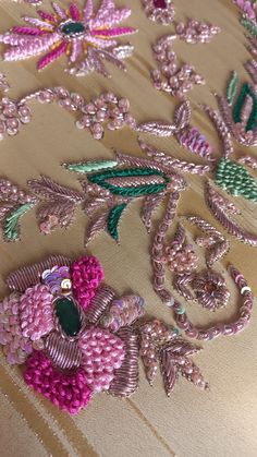 an embroidered piece with pink flowers and green leaves on a tan background, surrounded by beads