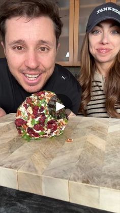 a man and woman sitting at a table with food in front of them on a cutting board