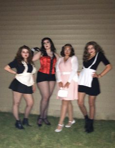 four young women posing for the camera in front of a wall and grass covered area