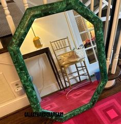 a green mirror sitting on top of a red rug next to a stair case and table