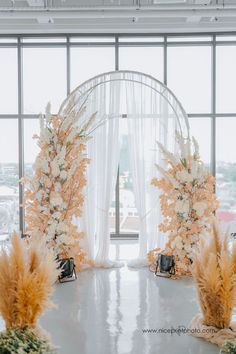 an arch decorated with flowers and pamodia stands in front of a large window