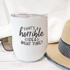 a white coffee mug with the words that's a horrible idea what time? on it next to a straw hat and sunglasses