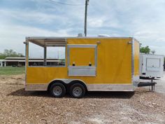 a yellow food truck parked in a parking lot next to a white trailer on gravel