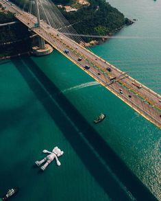 an aerial view of a bridge over water with boats in the foreground and cars driving on it