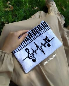 a woman is holding a white and black purse with musical notes on it, while sitting in the grass