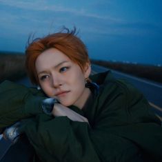 a woman with red hair is leaning on the side of a car and looking at the camera