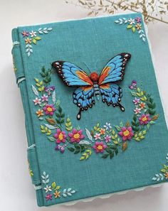 a blue book with a butterfly on the cover and flowers around it, sitting on a table