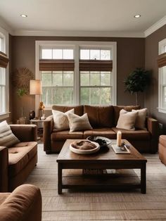 a living room with couches, tables and two windows in the wall behind them