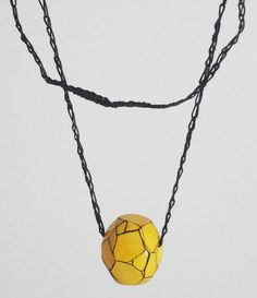 a necklace with a yellow ball hanging from it's side on a black chain