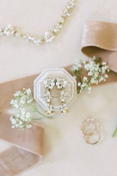 wedding rings and flowers on the ground with ribbons, pearls, and beads around them