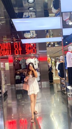 a woman in a white dress is looking at her cell phone while walking through a clothing store