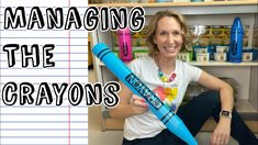 a woman holding a giant blue crayon in front of a shelf with writing on it