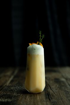 a drink sitting on top of a wooden table next to a black background with an orange garnish