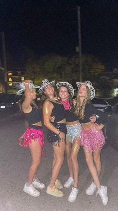 three girls in costumes standing next to each other on the street at night with their arms around one another