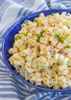 a blue bowl filled with macaroni salad on top of a striped table cloth