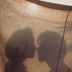 the shadow of two people in front of a sheered sheet with flowers on it