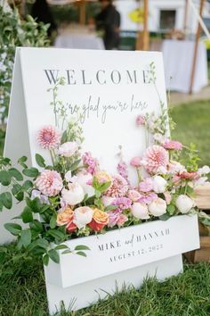 a welcome sign with flowers and greenery on the grass in front of a tent