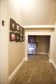 an empty hallway with bookshelves and pictures on the wall