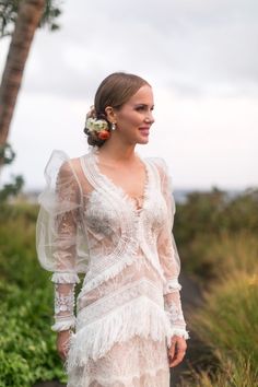 a woman in a white dress standing next to a palm tree and wearing a flower in her hair