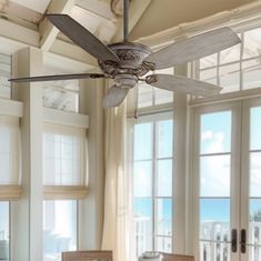 a ceiling fan is hanging in front of two large windows with french doors leading to the beach