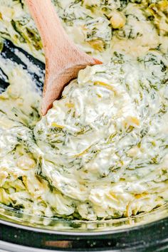 a wooden spoon mixing spinach dip in a crock pot