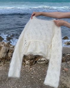 a woman is holding up a white sweater on the beach by the water's edge