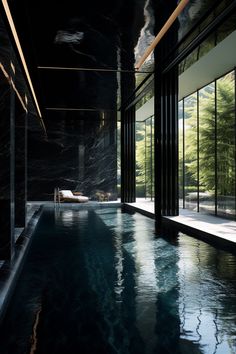 an indoor swimming pool surrounded by glass walls and floor to ceiling windows with trees in the background