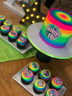 cupcakes are sitting on trays next to a rainbow cake and other decorations