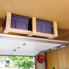 two purple bins sitting on top of a wooden shelf above a garage door,