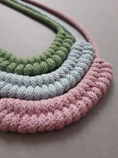 four crocheted necklaces are arranged on a gray surface, one is green and the other is pink