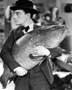 a man in a suit and hat holding a large fish