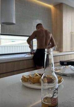 a man standing in the kitchen behind a bottle of beer