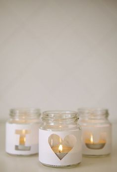 three mason jars with candles in the shape of a heart are on a white surface