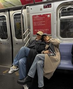 two people sitting on a subway car with their arms around each other's shoulders