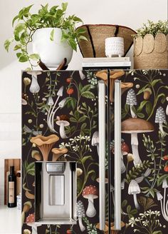 a refrigerator covered in wallpaper with mushrooms and plants on the front, next to a potted plant