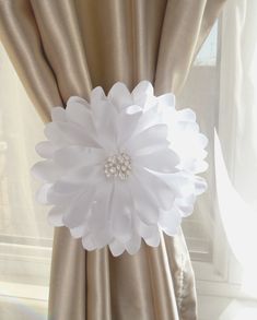 a white flower sitting on top of a window sill next to a drapes