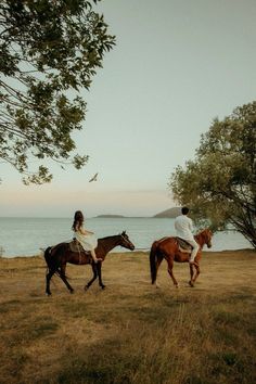 two people are riding horses near the water