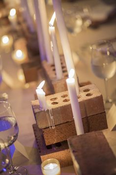 candles are lit on small brick blocks in the center of a table with wine glasses