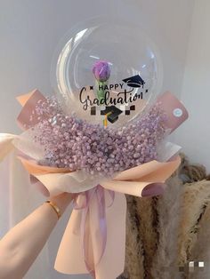 a person holding a clear bubble filled with purple flowers and congratulations written on the front