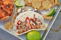 a tray filled with tacos and chips next to a lime