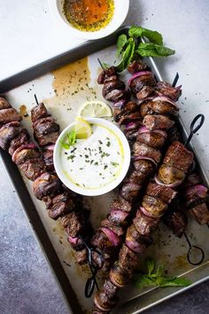 several skewers of meat on a tray with dipping sauce and lemon wedges