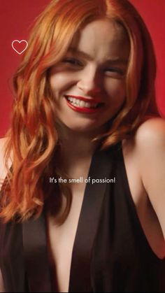 a woman with red hair smiling and wearing a black dress that says it's the smell of passion