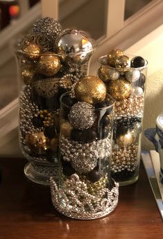 three glass vases filled with ornaments on top of a wooden table next to a window