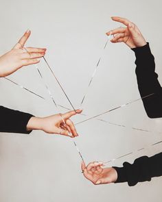 four hands are trying to pull the strings off of each other's fingers with their fingertipss