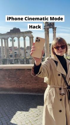 a woman taking a selfie with her phone in front of an ancient roman structure