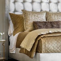 a bed with gold comforter and pillows on top of it next to a night stand