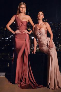 two women standing next to each other wearing evening dresses in front of a cityscape