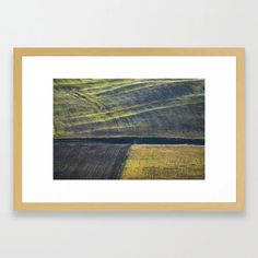 an abstract landscape with green and yellow colors framed in a wooden frame on a wall