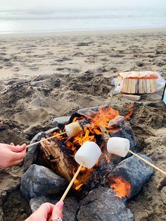 someone roasting marshmallows over an open fire on the beach